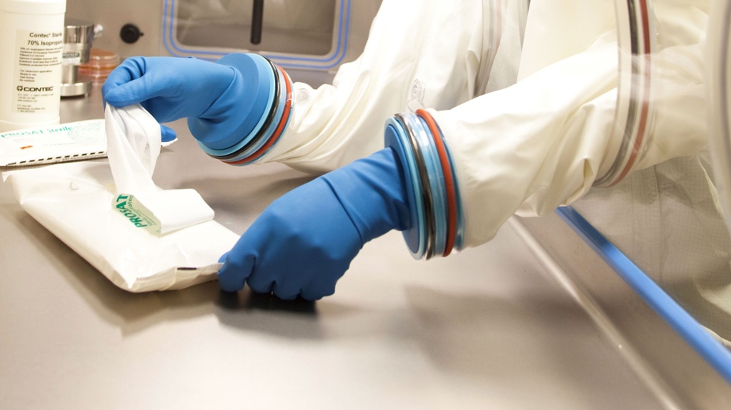 gloved hands in a glass container grabbing contec wipes